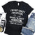 Black t-shirt with humorous text design on a wooden surface with shoes and jeans.