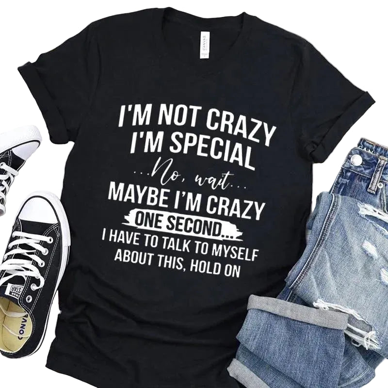 Black t-shirt with humorous text design on a wooden surface with shoes and jeans.