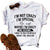 White t-shirt with humorous text design on a wooden surface with sandals and jeans.