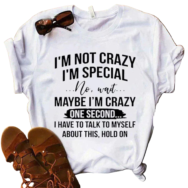 White t-shirt with humorous text design on a wooden surface with sandals and jeans.